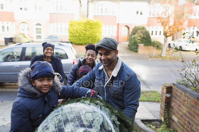 Porträt glückliche Familie trägt Weihnachtsbaum in Einfahrt — Stockfoto