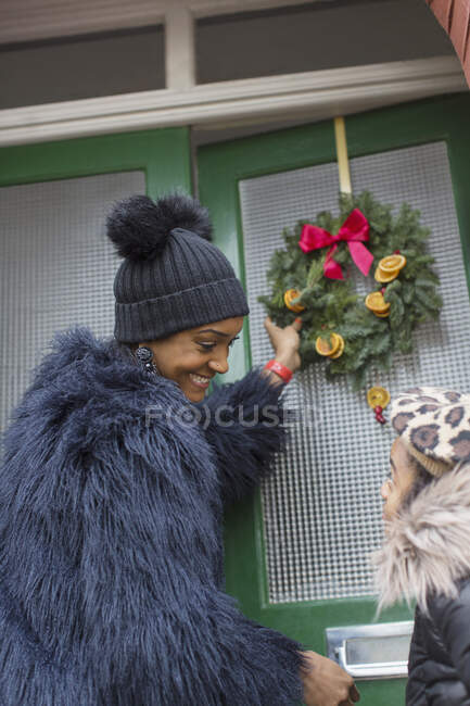 Feliz madre e hija colgando corona de Navidad en la puerta principal - foto de stock