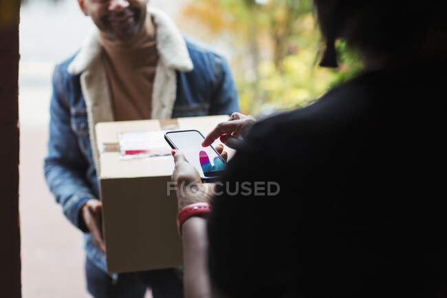 Mulher assinando digitalmente telefone inteligente para o pacote na porta da frente — Fotografia de Stock