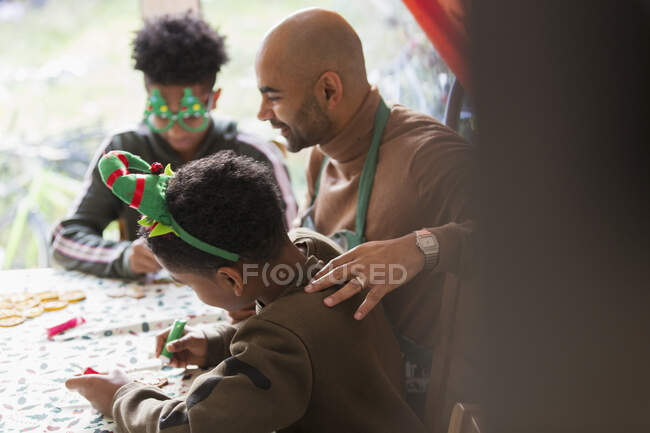 Отец и сыновья украшают рождественское печенье за столом — стоковое фото