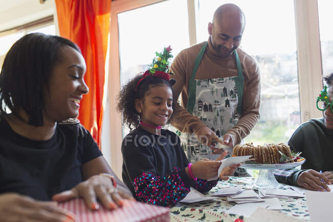 Familia feliz envolviendo regalos de Navidad y tarjetas de escritura en la mesa - foto de stock