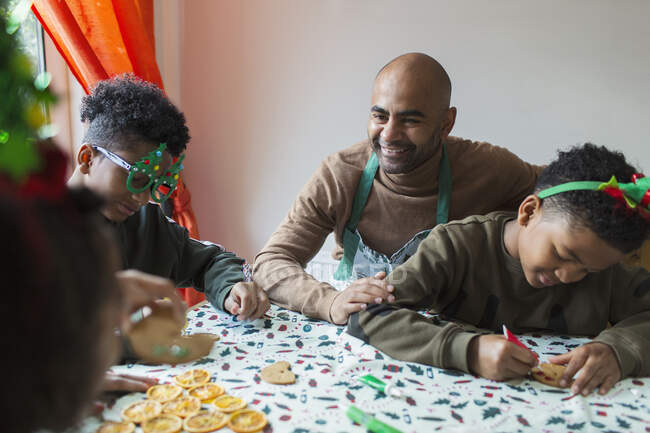 Pai feliz e filhos que decoram biscoitos de Natal à mesa — Fotografia de Stock