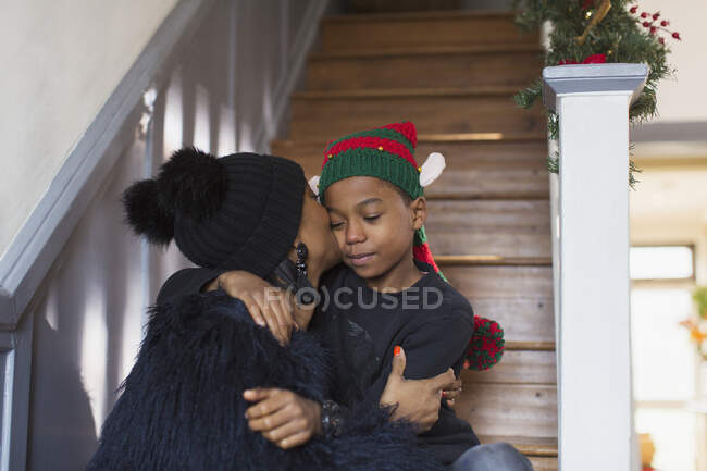 Zärtliche Mutter küsst Sohn mit Weihnachtsmütze auf Treppe — Stockfoto