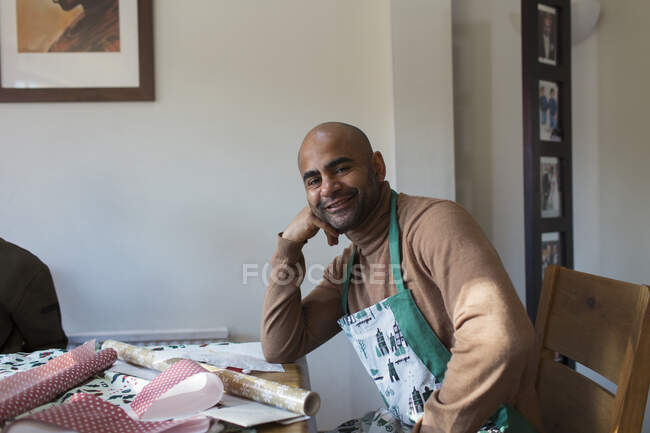 Portrait happy man in Christmas apron wrapping gifts at table — Stock Photo
