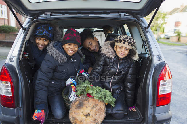 Retrato hermanos felices y hermana con árbol de Navidad en la parte trasera del coche - foto de stock