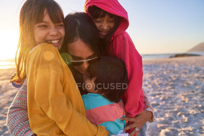 Madre feliz y niños abrazándose en la playa soleada - foto de stock