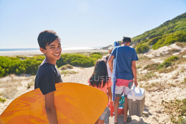 Портрет щасливого хлопця, який несе дошку на сонячному пляжі з родиною. — стокове фото