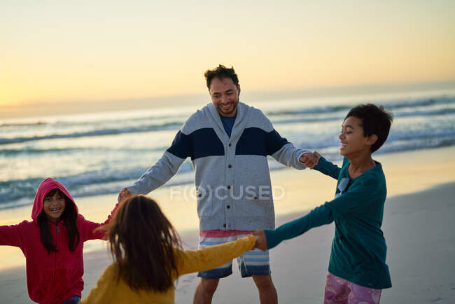 Happy father and kids holding hands in circle on sunset beach — Stock Photo