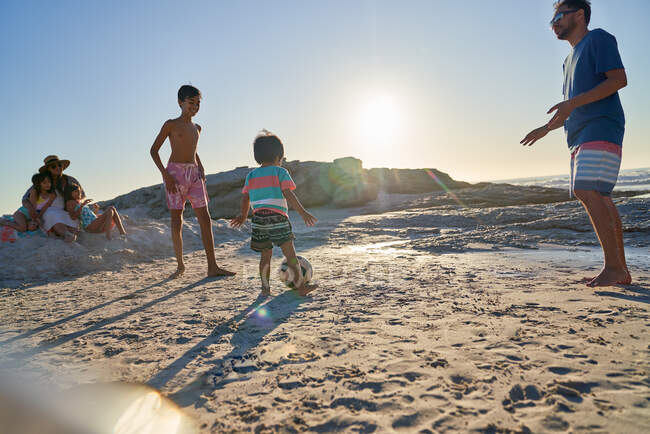 Famille jouant au football sur la plage ensoleillée — Photo de stock