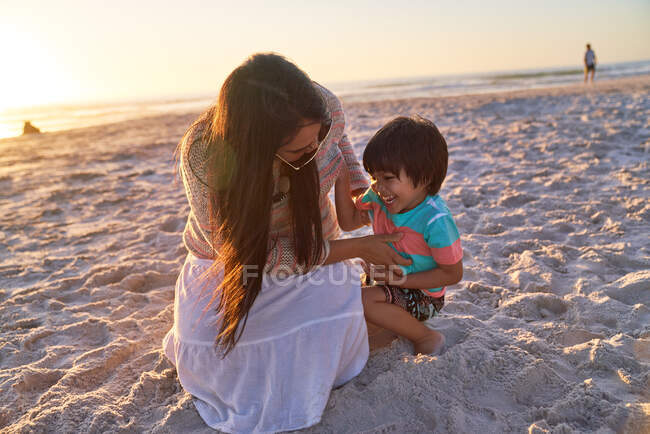 Mère ludique chatouillant fils sur la plage du coucher du soleil — Photo de stock