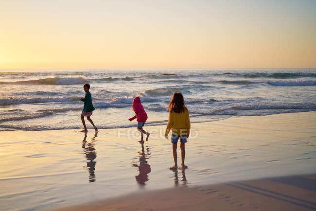 Frères et sœurs qui courent dans le surf au coucher du soleil — Photo de stock