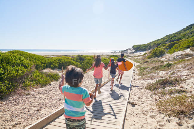 Hermanos y hermanas corriendo en el soleado paseo marítimo de la playa - foto de stock