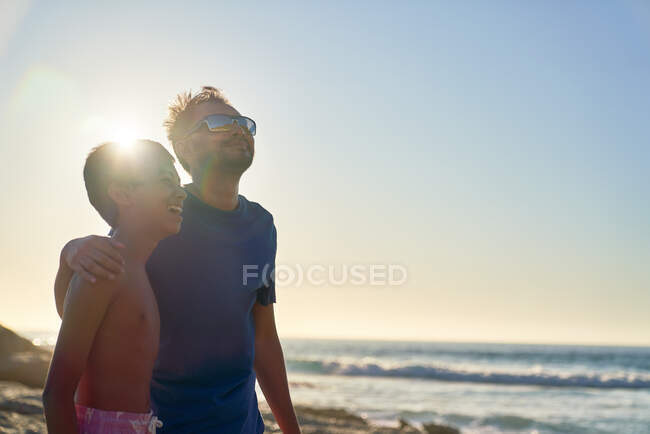 Любящий отец и сын обнимаются на солнечном берегу океана — стоковое фото