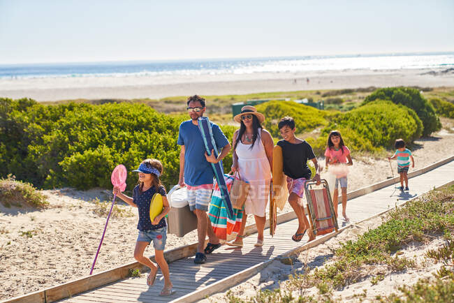 Familia que lleva sillas y juguetes en el paseo marítimo soleado de la playa - foto de stock