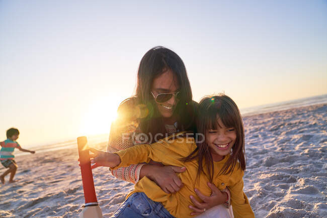 Щаслива мати і дочка обіймаються на сонячному пляжі заходу сонця — стокове фото