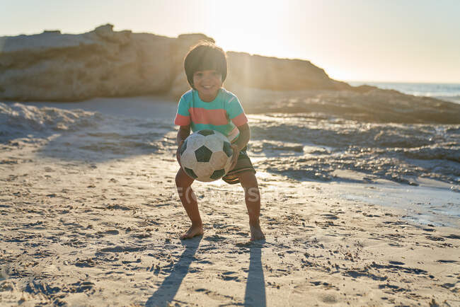 Ritratto carino ragazzo che gioca con pallone da calcio sulla spiaggia soleggiata — Foto stock