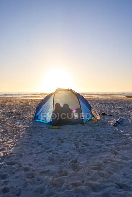 Família silhueta dentro da tenda na ensolarada praia do pôr do sol — Fotografia de Stock