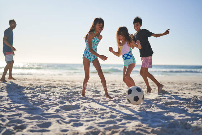 Família feliz jogando futebol na praia ensolarada — Fotografia de Stock