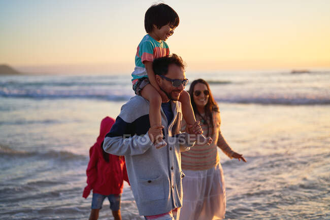 Familia feliz vadeando en el océano al atardecer - foto de stock