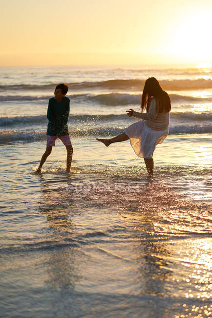 Glückliche Mutter und Sohn planschen bei Sonnenuntergang in der Brandung des Ozeans — Stockfoto