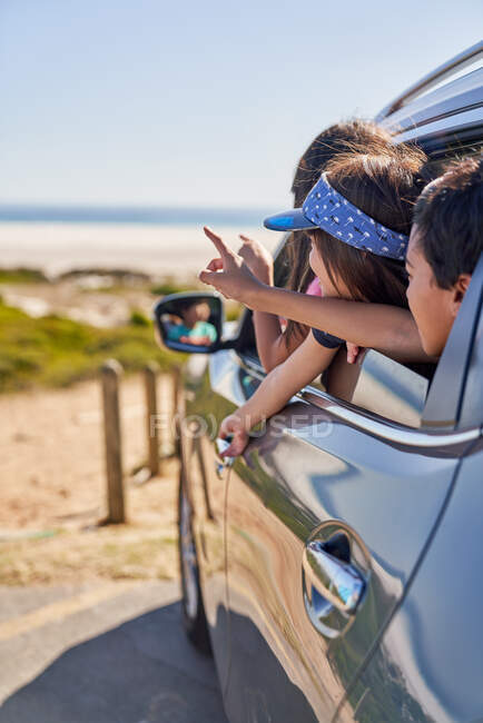 Niños felices asomándose por la ventana del coche en la playa - foto de stock