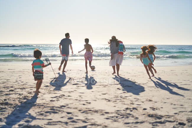Familie läuft und spielt Fußball am sonnigen Ozeanstrand — Stockfoto