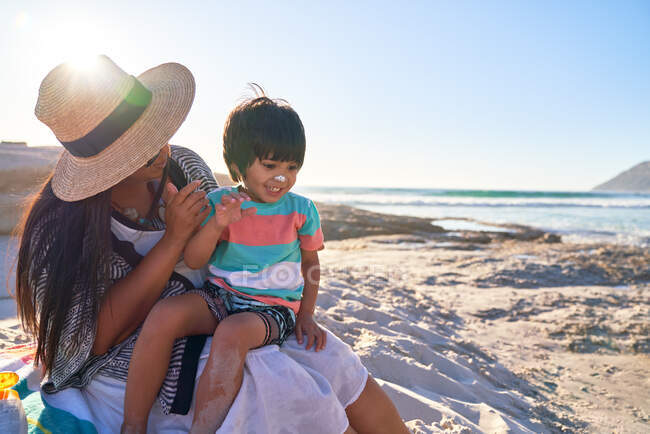 Мама намазывает солнцезащитный крем на нос милого сына на солнечном пляже — стоковое фото