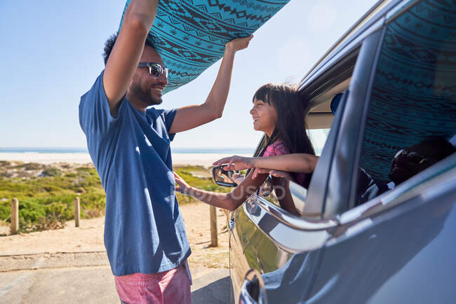 Filha assistindo pai remover a prancha de surf do carro na praia ensolarada — Fotografia de Stock