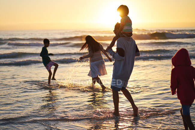 Familie spielt und planscht in der Brandung des Ozeans bei Sonnenuntergang — Stockfoto