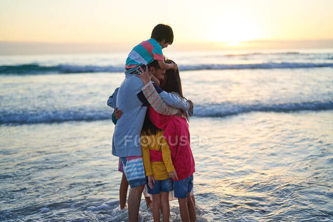 Glückliche, liebevolle Familie, die sich bei Sonnenuntergang in der Brandung des Ozeans umarmt — Stockfoto