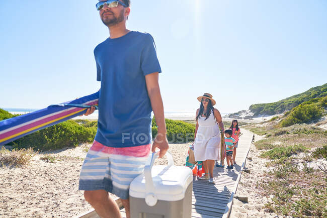 Famille portant équipement de plage sur la promenade ensoleillée — Photo de stock