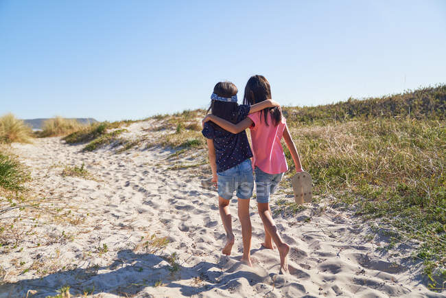 Happy affectionate sisters walking on sunny beach — Stock Photo