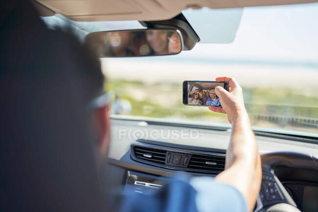Famiglia in viaggio prendendo selfie con fotocamera telefono in auto soleggiata — Foto stock