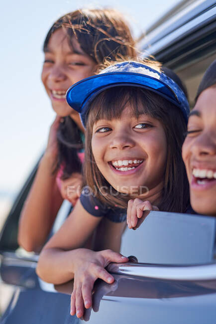 Happy sisters and brother leaning out sunny car window — Stock Photo