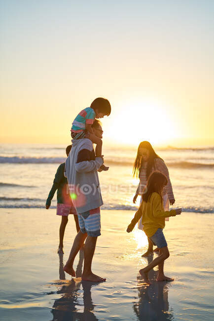 Famille pataugeant dans l'océan surfer sur la plage ensoleillée au coucher du soleil — Photo de stock