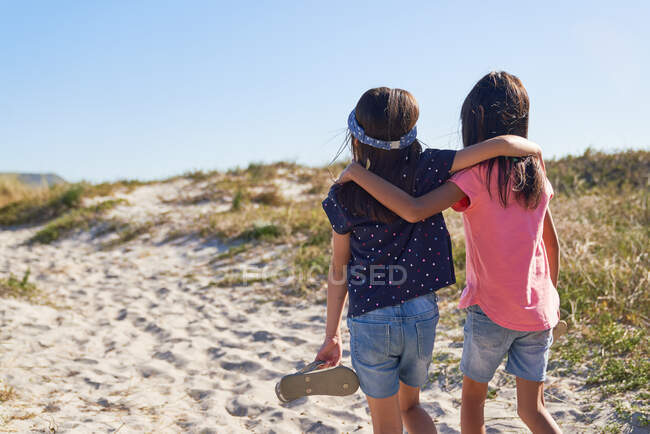 Ласковые сестры, идущие по солнечному пляжному пути — стоковое фото