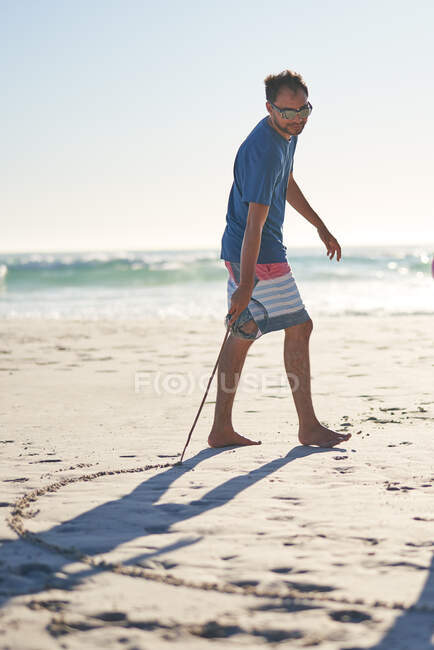 Homem desenhando na areia com pau na praia ensolarada — Fotografia de Stock