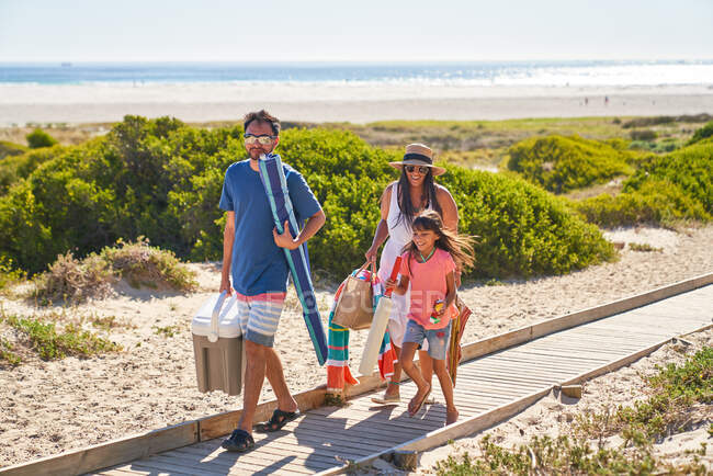 Familia feliz caminando en el paseo marítimo soleado de la playa - foto de stock