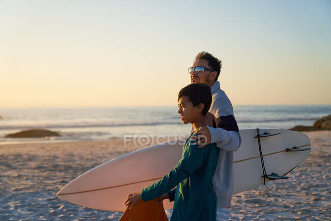 Отец и сын с доской для серфинга на солнечном пляже — стоковое фото