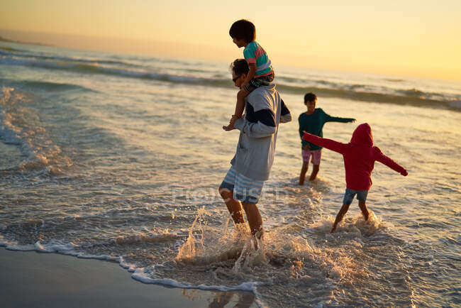 Éclaboussures de famille et de jouer dans le surf de l'océan au coucher du soleil — Photo de stock