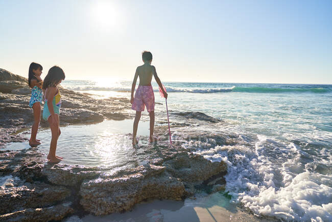 Brother and sisters playing in tide pool on sunny ocean beach — Stock Photo