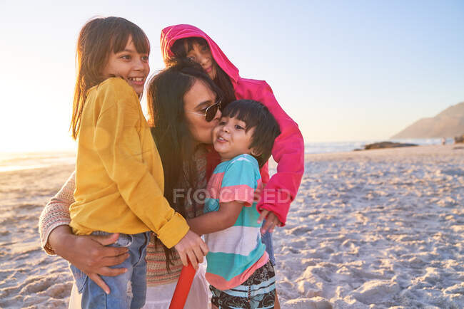 Affettuosa madre baciare i bambini sulla spiaggia soleggiata — Foto stock