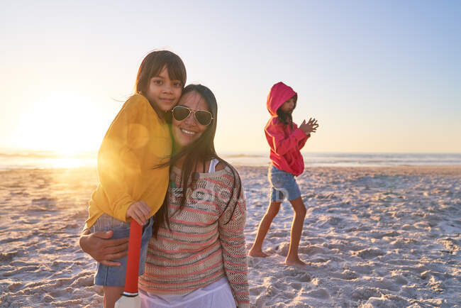 Portrait happy mother and daughters on sunny beach at sunset — Stock Photo