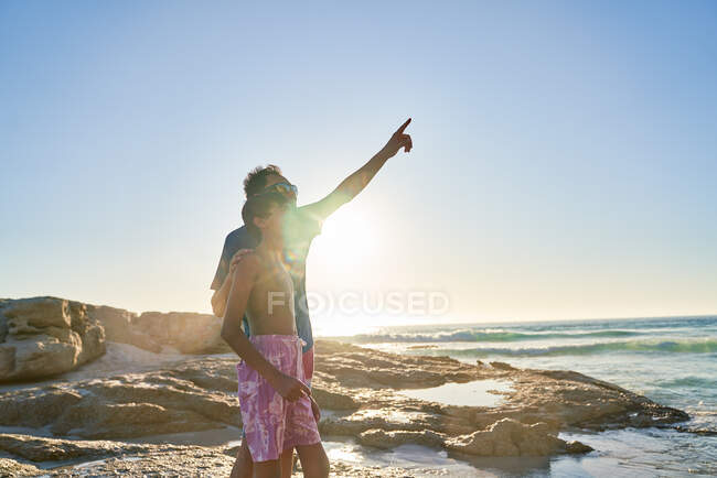 Pai e filho apontando para o céu na ensolarada praia oceânica — Fotografia de Stock
