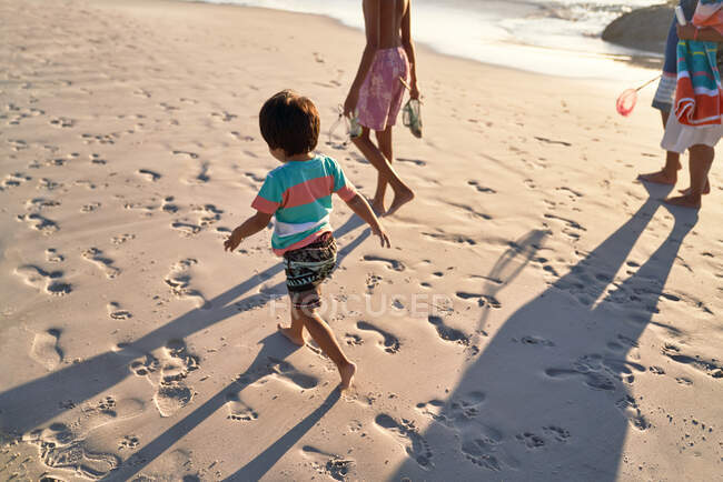 Симпатичный мальчик бегает по пляжу с семьей — стоковое фото