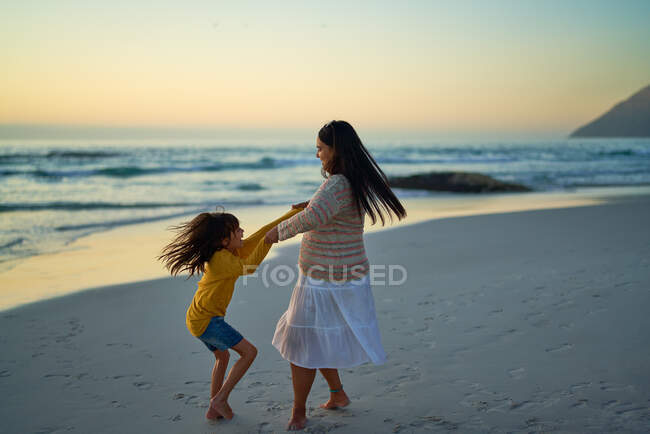 Счастливые мать и дочь кружатся на океанском пляже на закате — стоковое фото
