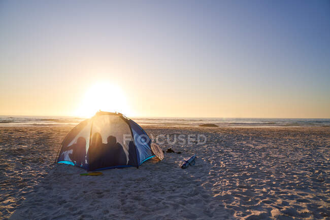 Silhouette of family inside tent on sunny beach at sunset — Stock Photo