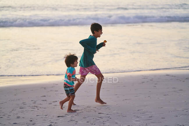 Счастливые братья бегут по океанскому пляжу — стоковое фото