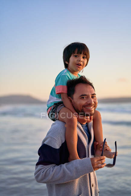 Portrait happy father carrying son on shoulders on beach — Stock Photo