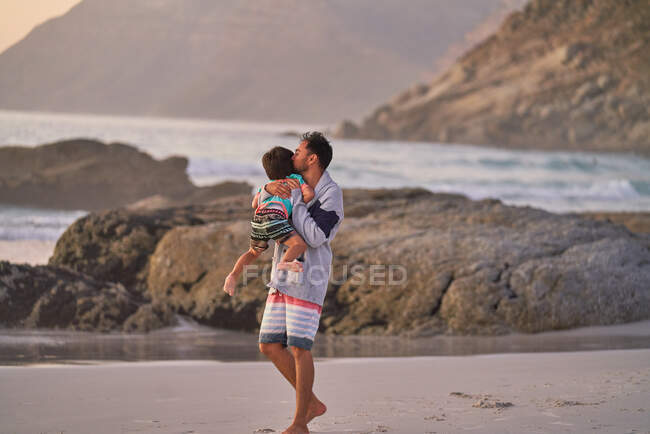 Carinhoso pai abraçando e beijando filho na praia do oceano — Fotografia de Stock